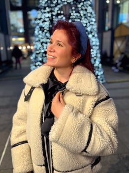 Millennial woman standing outdoors at Christmas night, wrapped in a cozy shearling jacket. the city lights in the background create a warm and Christmas holidays atmosphere, photo