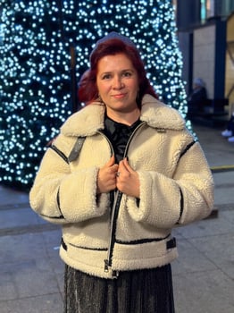 Millennial woman standing outdoors at Christmas night, wrapped in a cozy shearling jacket. the city lights in the background create a warm and Christmas holidays atmosphere, photo