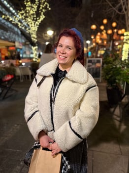 Millennial woman standing outdoors at Christmas night, wrapped in a cozy shearling jacket. the city lights in the background create a warm and Christmas holidays atmosphere photo