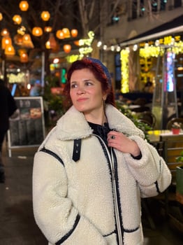 Millennial woman standing outdoors at Christmas night, wrapped in a cozy shearling jacket. the city lights in the background create a warm and Christmas holidays atmosphere photo