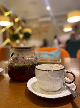 Delicate teacup alongside a clear teapot with blooming herbal tea captures a cozy tea time in a stylish, modern cafe. Inviting ambiance is highlighted by warm lighting and contemporary decor. photo