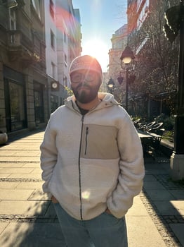 Millennial man stands confidently on a sunlit city street, wearing a cozy jacket and stylish hat. Urban landscape and soft morning light create a scene of casual elegance and modern lifestyle photo