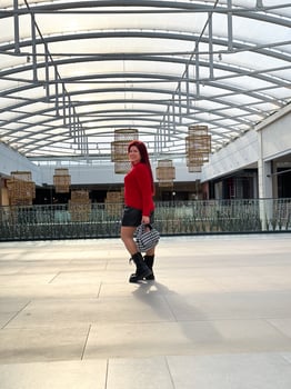 Millennial woman poses confidently in an open, modern environment, wearing a vibrant red sweater and black boots. photo