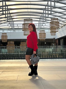 Millennial woman poses confidently in an open, modern environment, wearing a vibrant red sweater and black boots. photo