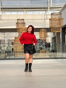 Millennial woman poses confidently in an open, modern environment, wearing a vibrant red sweater and black boots. photo