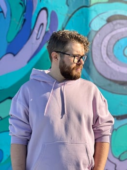 Millennial man in a pastel hoodie standing in front of a vibrant, abstract mural. Soft fabric and bold graffiti creates a striking contrast of modern urban style. Street urban style fashion photo