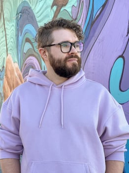 Millennial man in a pastel hoodie standing in front of a vibrant, abstract mural. Soft fabric and bold graffiti creates a striking contrast of modern urban style. Street urban style fashion photo