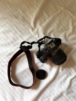 Camera with a strap placed on a white bed sheet, capturing the essence of travel preparation and creativity. Simplicity, creative and readiness of a photographer journey. Top view photo