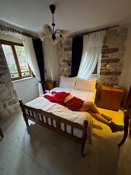 Millennial woman in a red sweater resting on a bed in a rustic bedroom with stone walls and white curtains. Moment of relaxation and comfort captured in a cozy setting in autumn photo