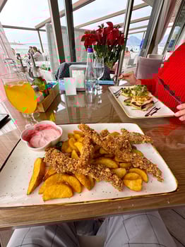 delicious meal is served on a glass table with a scenic view in the background, featuring crispy battered food and vibrant garnishes. a bright orange drink complements the setting photo