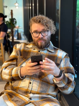 Millennial man with curly hair and glasses is focused on his smartphone while sitting in a cozy cafe. Social networks, communication and technologies concept photo