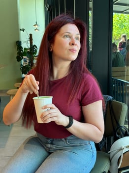 Woman with long red hair enjoys a casual moment at a coffee shop. Girl drink coffee in cafe. Bright interior and large windows create a cozy and inviting atmosphere. Breakfast time photo