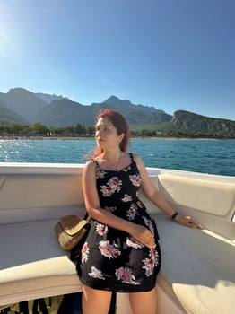 Woman in a black dress sits on a boat under the bright sun, with a scenic view of mountains and the sea in the background. Moment of tranquility and natural beauty concept. Vacation, travel and voyage photo