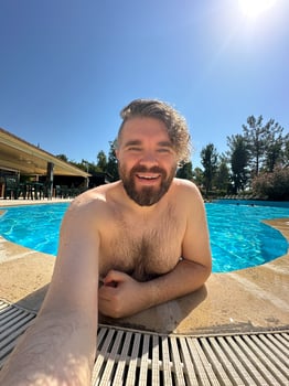 Millennial man taking selfie by swimming pool. Vibrant blue water and relaxed setting create a perfect atmosphere for summer fun. Holidays and vacation concept photo