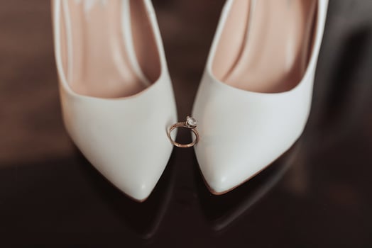 A pair of white shoes with a diamond ring on the left shoe photo
