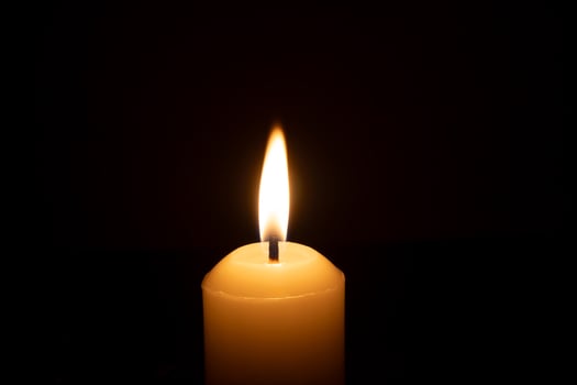 A single burning candle flame or light glowing on a big white candle isolated on red or dark background on table in church for Christmas, funeral or memorial service photo