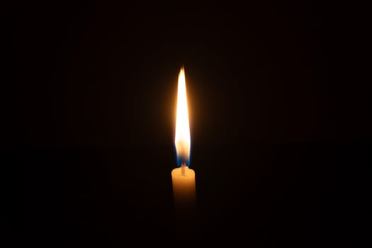 A single burning candle flame or light glowing on a small orange candle on black or dark background on table in church for Christmas, funeral or memorial service with copy space photo