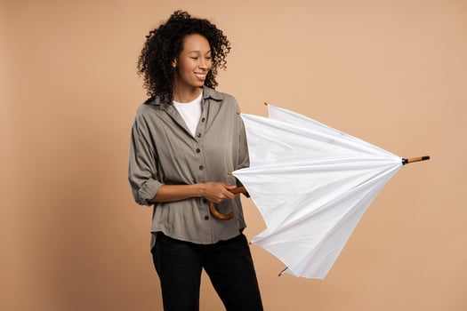 Smiling pretty African American woman opening white umbrella isolated on beige background photo