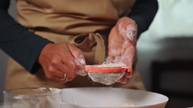 Home baker sifting flour into a bowl preparing delicious homemade cake in a cozy kitchen with a rustic feel photo