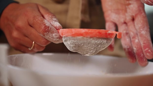 Close-up of hands sifting flour for homemade pumpkin cake preparation in the kitchen, showcasing baking process and homemade cooking with focus on ingredients and culinary techniques. photo