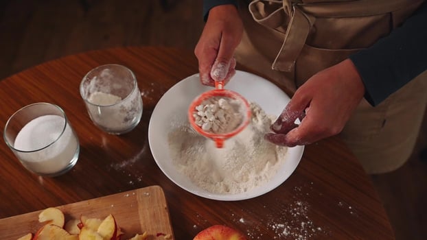 Person in dark clothing sifting flour into a white bowl on a wooden table while preparing to bake a pumpkin cake photo