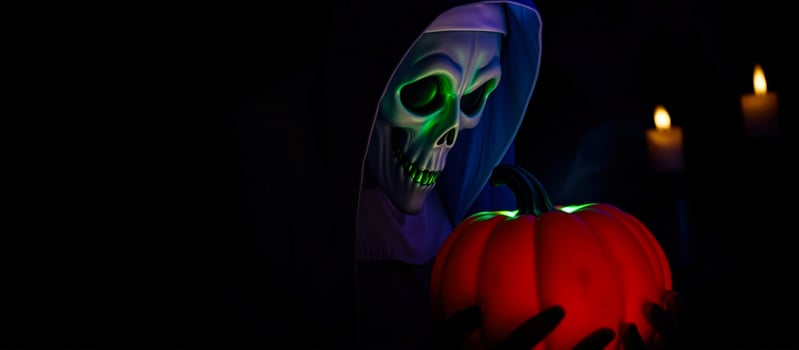 person wearing a skull mask holds a glowing red pumpkin photo