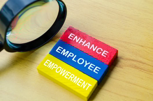 Top view of Enhance Employee Empowerment text on multicolored wooden blocks with magnifying glass background. Empowerment concept. photo