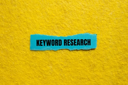 Keyword research message written on ripped torn blue paper piece with yellow background. Conceptual keyword research symbol. Copy space. photo