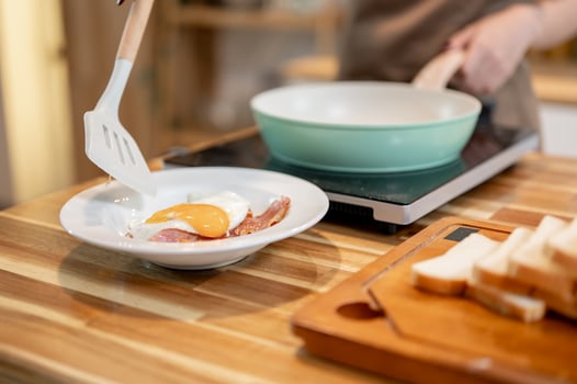 A close-up of a woman placing a fried egg on a plate on top of fried bacon, cooking in the kitchen. photo