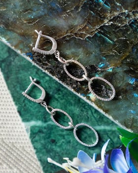 Pair of silver earrings with oval links lying on green marble slab photo