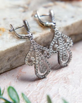 Pair of silver diamond earrings resting on stone surface photo