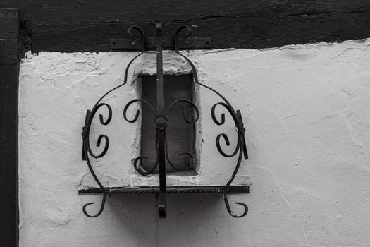 An intricate, black metal window frame is attached to a white building photo