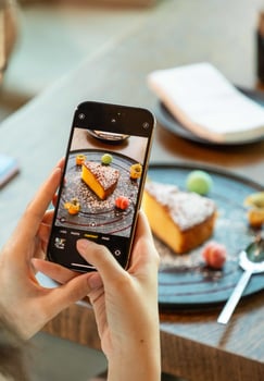 Woman taking photo of cake using smartphone in restaurant