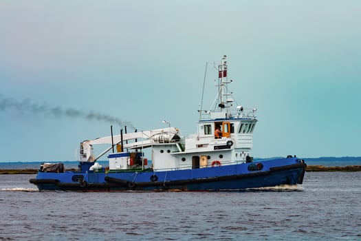 Blue tug ship moving to the cargo terminal. Industrial services photo