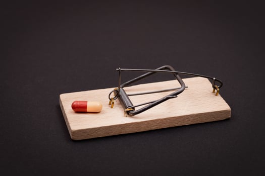 Pharmaceutical Addiction or Big Pharma Trap - Colored Pill or Capsule in Wooden Mousetrap on Black Background photo