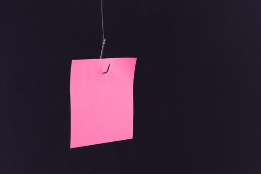 Mockup of a Blank Pink Memo Paper with Copy Space Hanging on a Fishing Hook Against the Black Background. Reminder or To Do List. Sticky Note Template photo