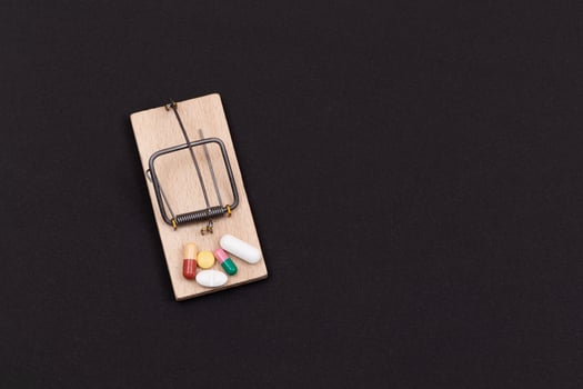 Pharmaceutical Addiction or Big Pharma Trap - Colored Pills or Capsules in Wooden Mousetrap on Black Background photo