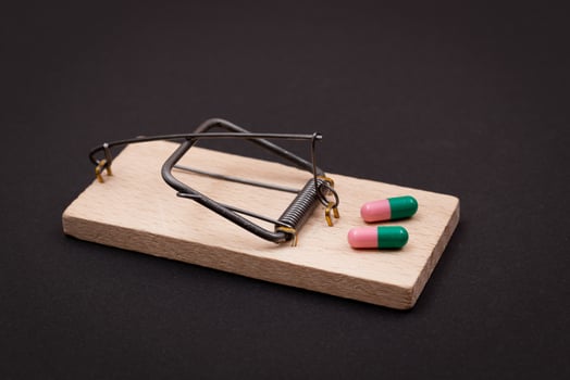 Pharmaceutical Addiction or Big Pharma Trap - Colored Pills or Capsules in Wooden Mousetrap on Black Background photo