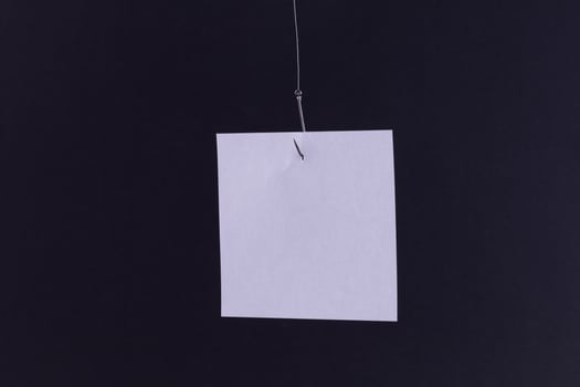 Mockup of a Blank White Memo Paper with Copy Space Hanging on a Fishing Hook Against the Black Background. Reminder or To Do List. Sticky Note Template photo