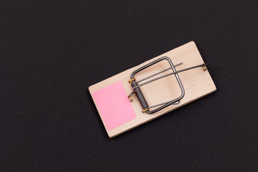 Blank Pink Sheet of Paper in Wooden Mousetrap - Template. Small Memo Paper in Mouse Trap on Black Background photo