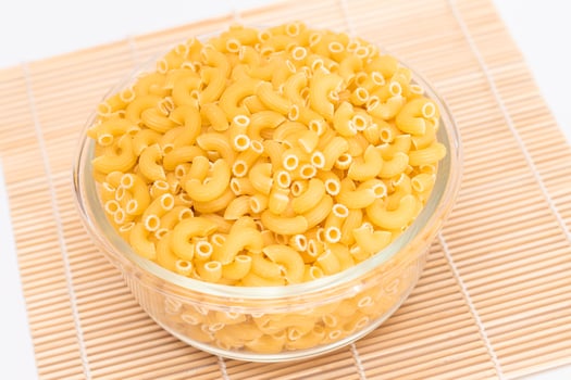 Uncooked Chifferi Rigati Pasta in Glass Jar on Bamboo Mat on White Background. Fat and Unhealthy Food. Classic Dry Macaroni. Italian Culture and Cuisine. Raw Pasta photo