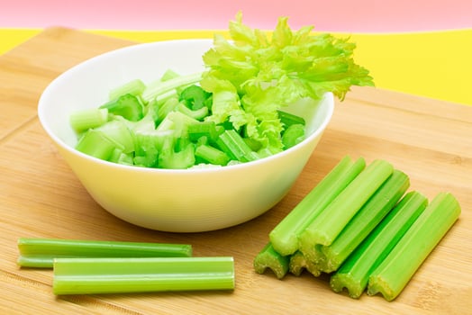 Fresh Chopped Celery Slices in White Bowl with Celery Sticks on Bamboo Cutting Board. Vegan and Vegetarian Culture. Raw Food. Healthy Diet with Negative Calorie Content photo
