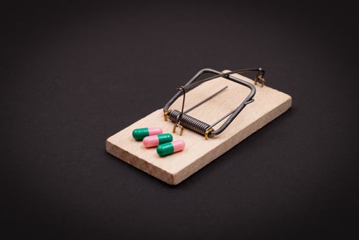 Pharmaceutical Addiction or Big Pharma Trap - Colored Pills or Capsules in Wooden Mousetrap on Black Background photo