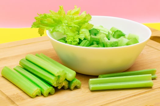 Fresh Chopped Celery Slices in White Bowl with Celery Sticks on Bamboo Cutting Board. Vegan and Vegetarian Culture. Raw Food. Healthy Diet with Negative Calorie Content photo