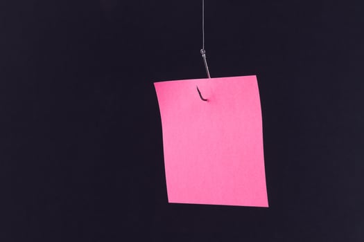 Mockup of a Blank Pink Memo Paper with Copy Space Hanging on a Fishing Hook Against the Black Background. Reminder or To Do List. Sticky Note Template photo