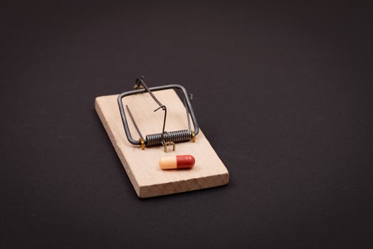 Pharmaceutical Addiction or Big Pharma Trap - Colored Pill or Capsule in Wooden Mousetrap on Black Background photo