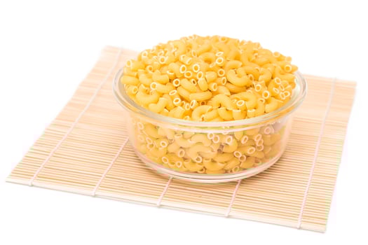 Uncooked Chifferi Rigati Pasta in Glass Jar on Bamboo Mat Isolated White Background. Fat and Unhealthy Food. Classic Dry Macaroni. Italian Culture and Cuisine. Raw Pasta - Isolation photo