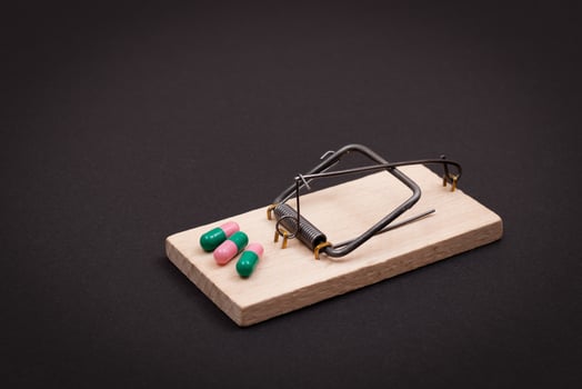 Pharmaceutical Addiction or Big Pharma Trap - Colored Pills or Capsules in Wooden Mousetrap on Black Background photo