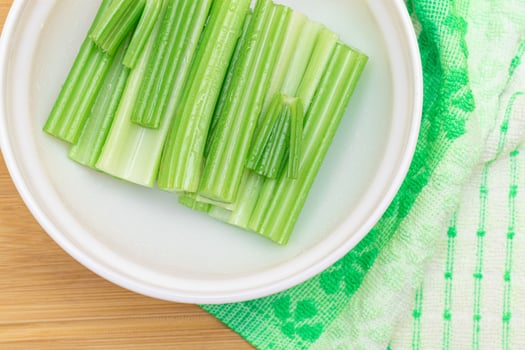 Fresh Chopped Celery Sticks with Water Drops in White Bowl on Bamboo Cutting Board - Top View. Vegan and Vegetarian Culture. Raw Food. Healthy Diet with Negative Calorie Content photo