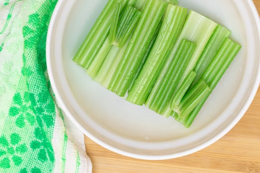 Fresh Chopped Celery Sticks with Water Drops in White Bowl on Bamboo Cutting Board - Top View. Vegan and Vegetarian Culture. Raw Food. Healthy Diet with Negative Calorie Content photo
